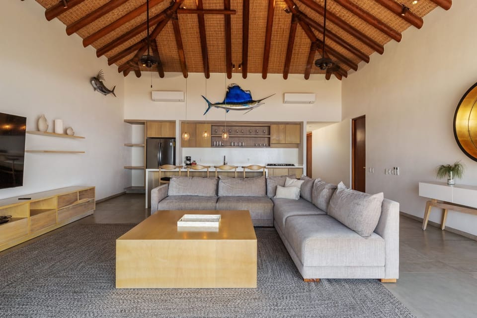 A warm and inviting living area with high ceilings, natural wood accents, and an open layout leading to the kitchen.