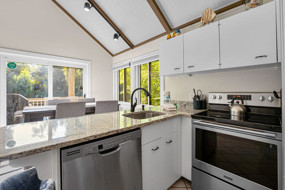 Open kitchen and dining space with granite counters, vaulted ceilings, and wooded views
