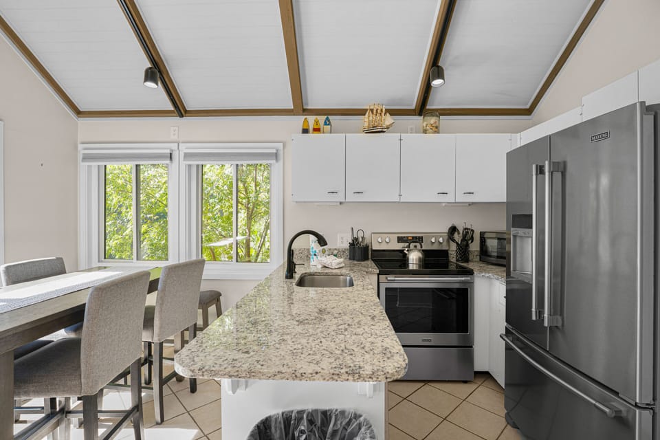 Bright kitchen and dining area with vaulted ceilings, granite countertops, and peaceful wooded views