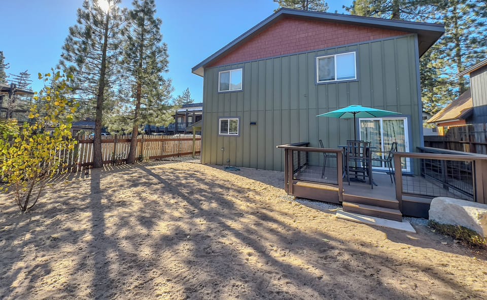 Two-story mountain retreat featuring outdoor deck with dining table and umbrella, surrounded by tall pines in a peaceful forest setting.