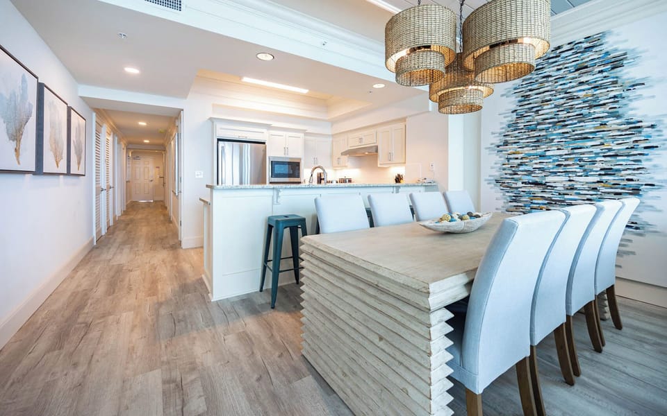 The dining area features stylish blue accents, and a view of the modern kitchen with stainless appliances