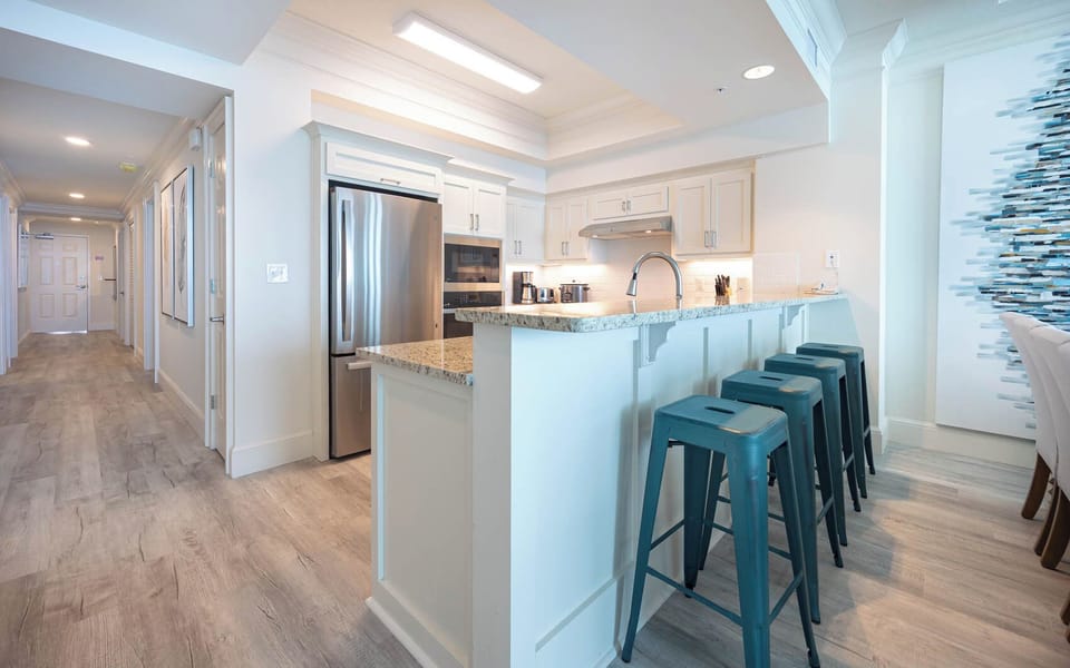 The modern kitchen features granite countertops, stainless appliances, and stylish teal bar stools for a welcoming atmosphere