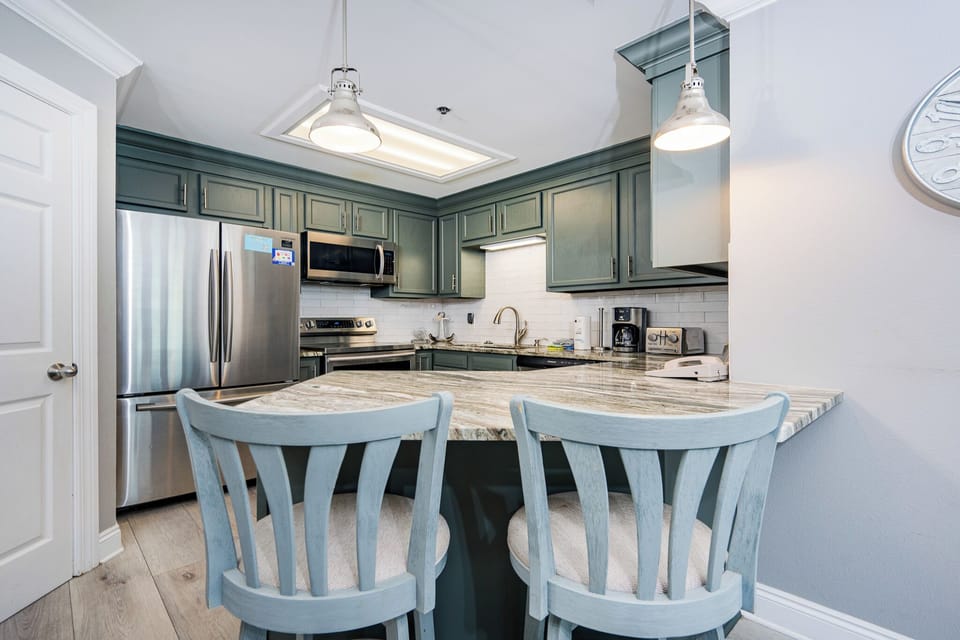 The kitchen features a breakfast bar with light blue stools, sleek cabinetry, stylish countertops, and stainless appliances