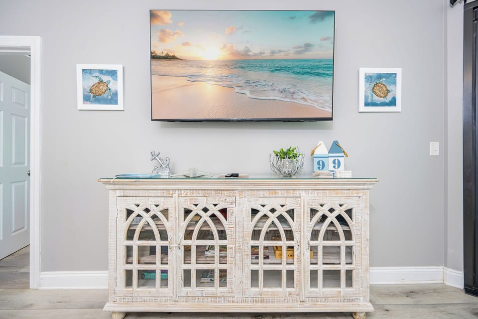 Coastal-themed decor features a white cabinet, framed sea turtle art, and a large TV in this living space