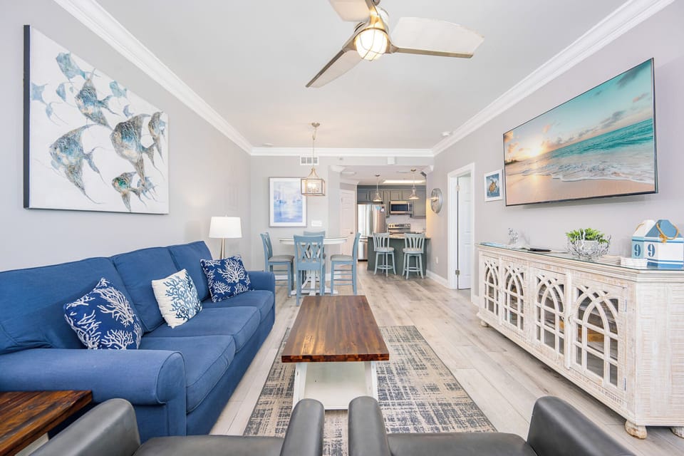 Living area features a blue sofa with queen sleeper, a wooden coffee table, and a view into the modern kitchen