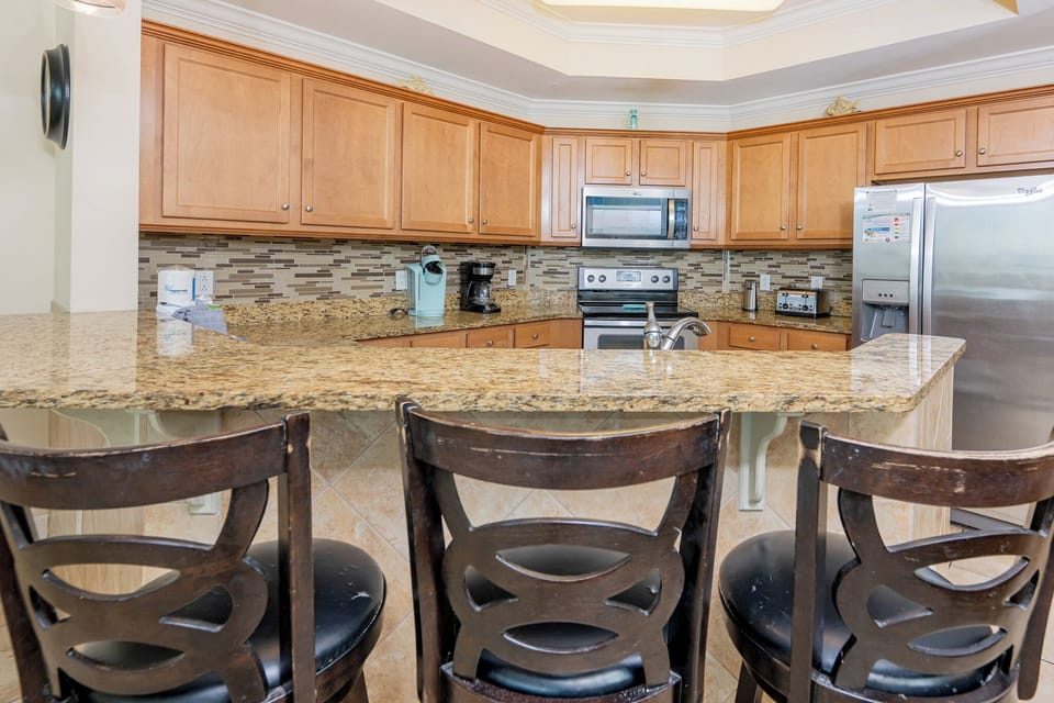 Inviting kitchen featuring granite countertops, stainless appliances, Keurig, coffee maker, and stylish bar seating