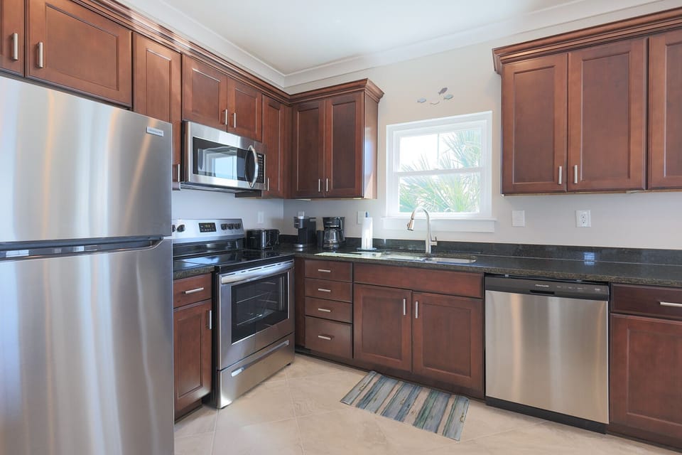 This kitchen features wooden cabinetry, stainless steel appliances, and a window view of lush greenery