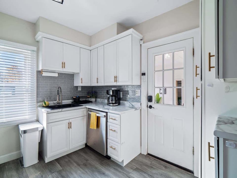 - Kitchen corner with dishwasher and sink station ready   - White cabinets with brass pulls add stylish contrast   - Access to backyard makes meal prep fresh and convenient  
