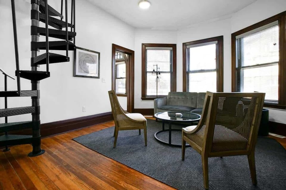 Sunlit sitting area w/ round table, chairs & spiral staircase nearby