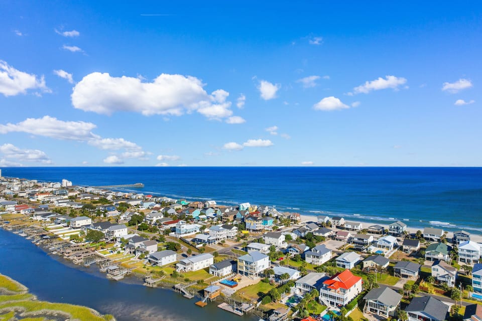 Stunning coastal community between bay and ocean, featuring diverse beachfront homes and pristine sandy shores under brilliant blue skies.