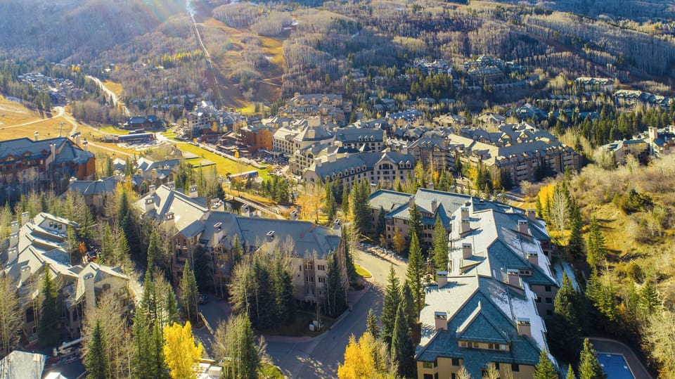 Aerial view of a mountain resort town with clusters of buildings, surrounded by trees and hilly terrain.