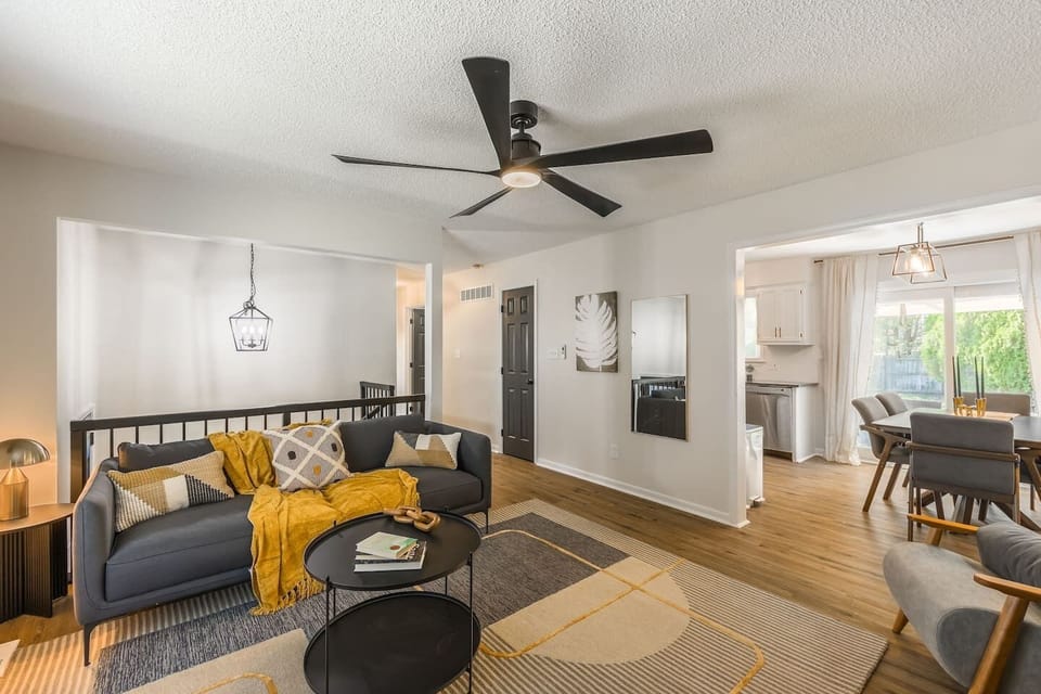 Bright and modern living area featuring stylish mid-century furniture, a large cozy sectional, and thoughtful decor accents. The space includes a flat-screen TV, lush greenery, and warm lighting, perfect for relaxing or entertaining.