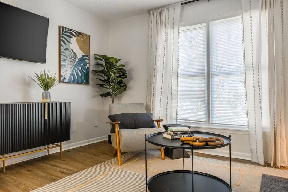 Bright and modern living area featuring stylish mid-century furniture, a large cozy sectional, and thoughtful decor accents. The space includes a flat-screen TV, lush greenery, and warm lighting, perfect for relaxing or entertaining.