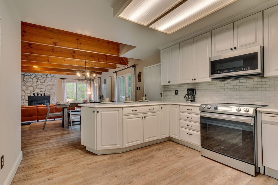 - Modern kitchen with stainless steel appliances and white cabinets  
- Open flow connects to dining and living with rustic beams  
- Fully equipped for family meals and mountain stays
