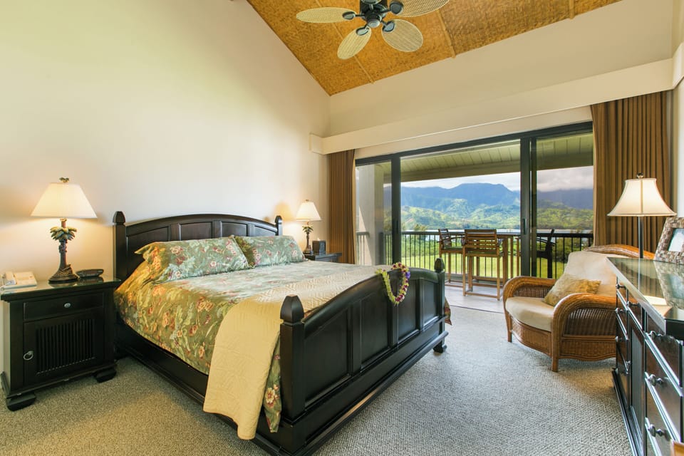 Spacious bedroom with a king-sized bed, elegant furnishings, and access to a private lanai offering breathtaking mountain views.