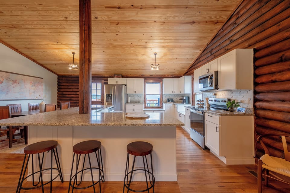 This inviting kitchen area highlights the modern design blended with rustic charm at Valley View Getaway. The spacious island with bar seating is perfect for casual meals or entertaining, while the high-end appliances and beautiful granite countertops make cooking a pleasure. Natural light floods in from the surrounding windows, illuminating the well-appointed kitchen and the a...
