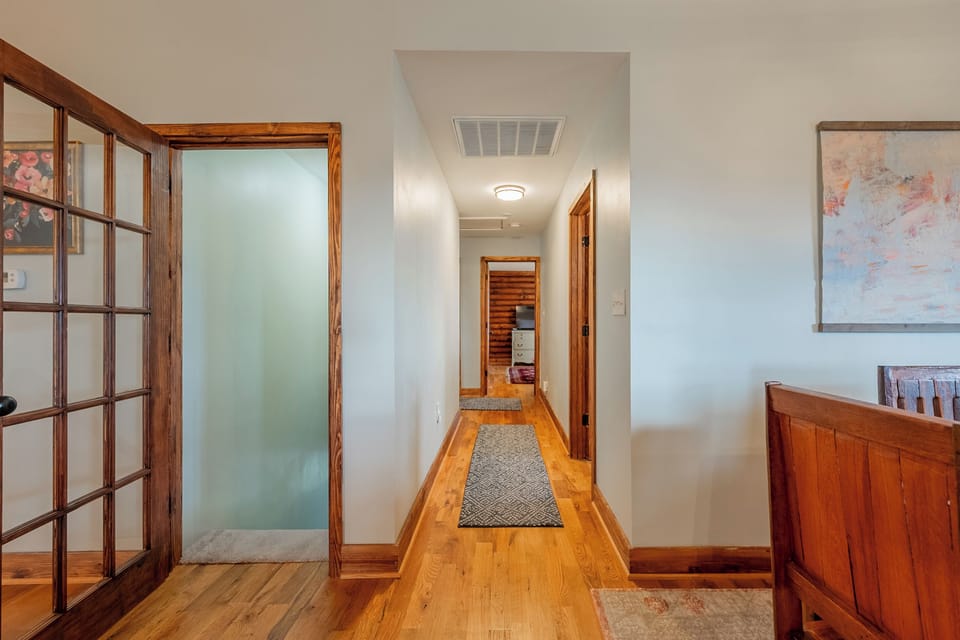 The well-lit hallway features a warm color palette and natural wood accents, leading guests effortlessly throughout Valley View Getaway. With tasteful decor and cozy rugs, this welcoming space offers a glimpse into the home's inviting atmosphere while providing access to the upstairs bedrooms and full hall bathroom.