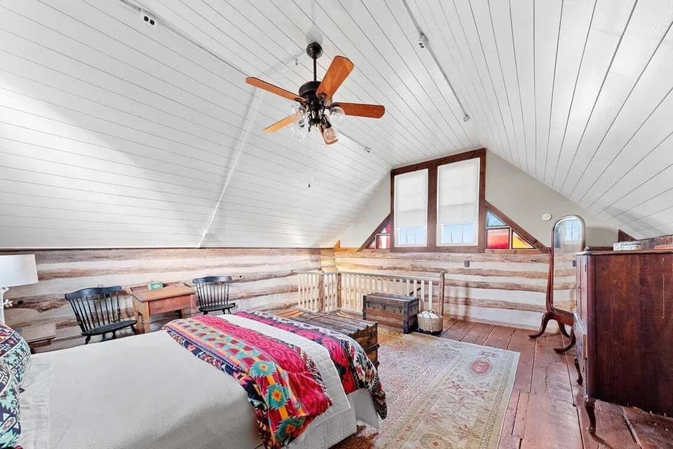 A reverse loft angle highlights the colorful bed, reading chair, wood flooring, and generous space beneath the vaulted ceiling.