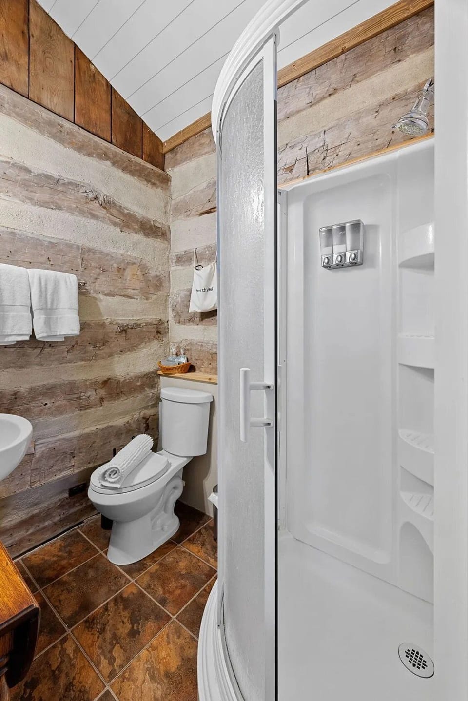 The private bathroom includes a glass-enclosed shower, toilet, vanity, fresh towels, and rustic log accents.