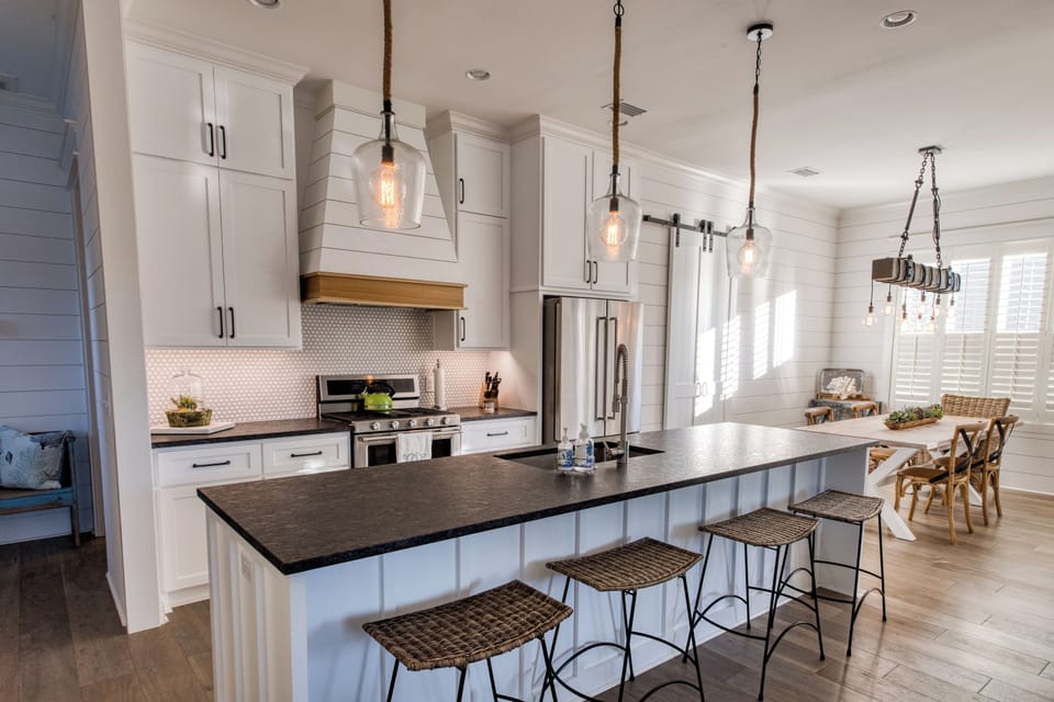 Kitchen With Island Seating And Gas Range - White cabinetry, a long island, bar stools, and the dining table keep meals and snacks easy on the main floor.