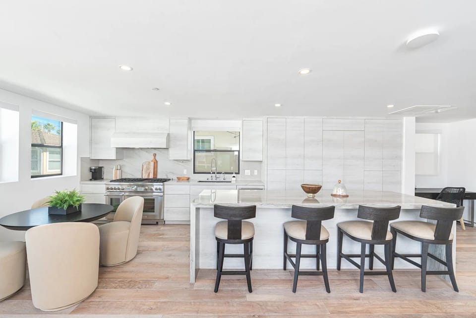 Bright, modern kitchen and dining space featuring high-end appliances, a spacious island, and contemporary seating
                