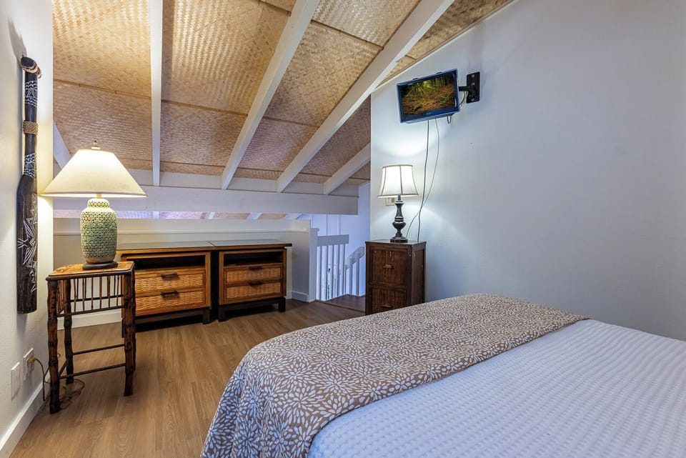 Unwind in your private retreat where natural woven ceilings meet island-inspired furnishings, creating a serene escape beneath the sloped beams that give this cozy bedroom its unique character.