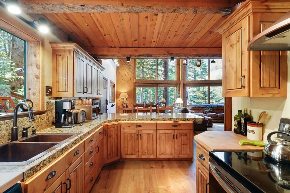 The kitchen features a granite bar table with high chairs, wooden cabinets, and kitchen appliances, all brightened by large glass windows.