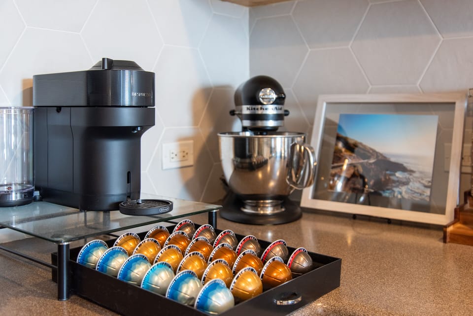 Nespresso coffee maker with various pods and KitchenAide stand mixer. French press also available.