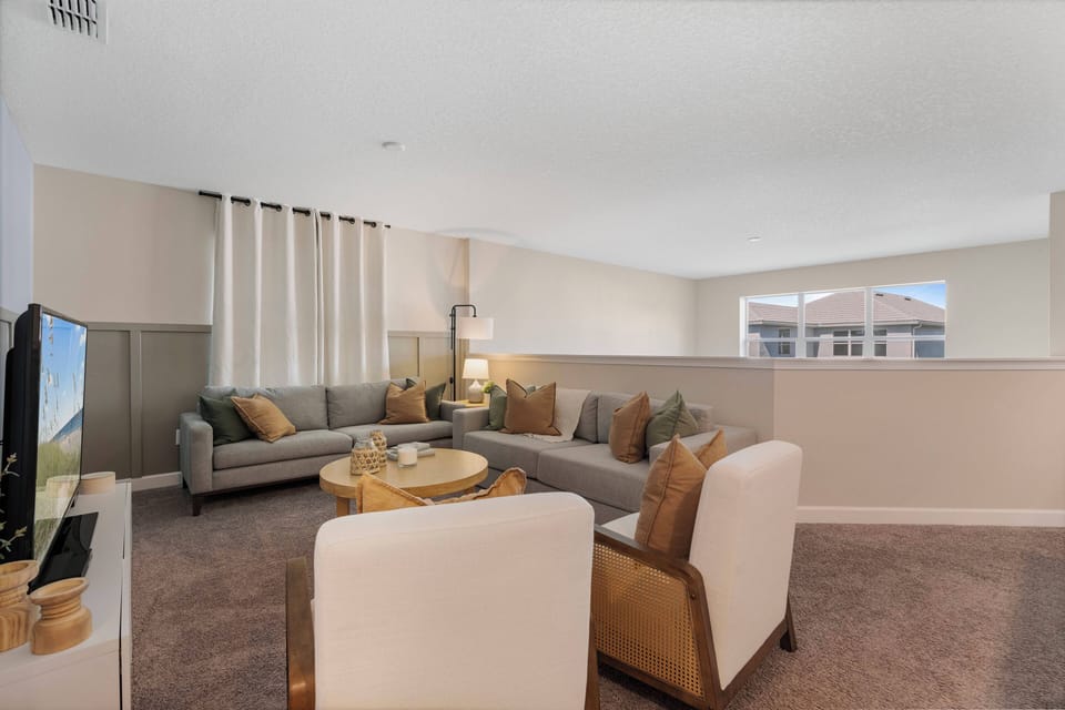 Relax in a spacious living room adorned with soft, earthy tones and plush seating. Large windows invite natural light, illuminating the cozy atmosphere, while a stylish coffee table serves as the perfect spot for gathering.