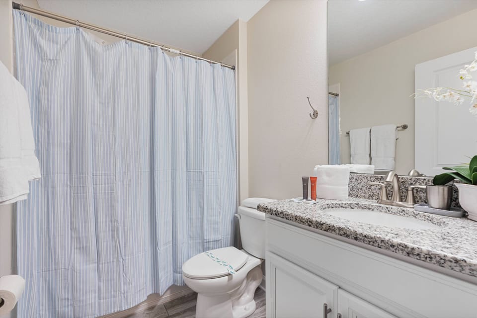 This stylish bathroom showcases a chic gray granite countertop and a calming blue and white striped shower curtain, creating a fresh atmosphere, while a touch of greenery adds a natural element for a tranquil feel.