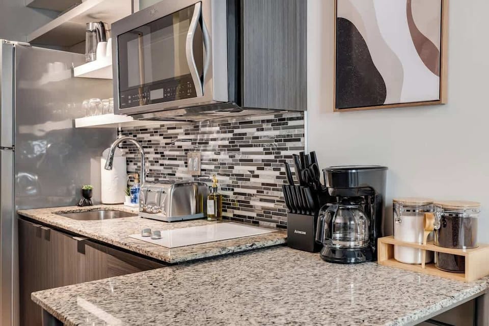 Modern kitchen with granite counters, backsplash, coffee maker, and essentials.