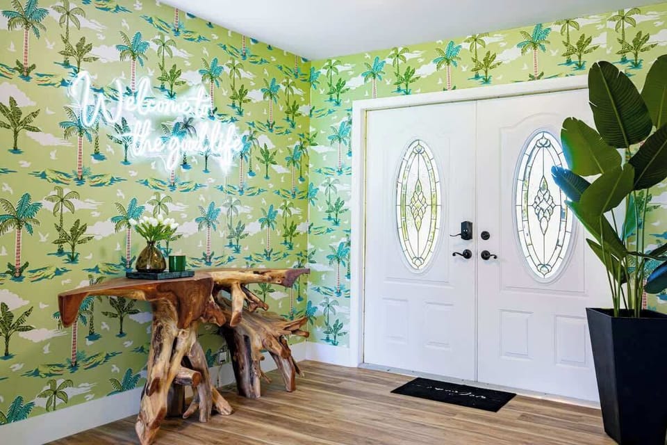  Welcome to the good life! Step into this vibrant foyer, where fun alligator wallpaper, chic wooden accents, and a touch of greenery set the tone for your stay.