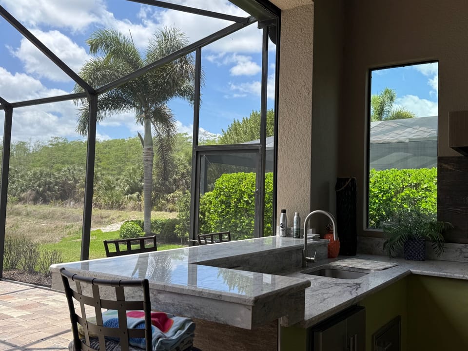Your screened outdoor kitchen offers tropical views while you prepare meals, with granite counters and lush palm trees creating the perfect Florida ambiance.