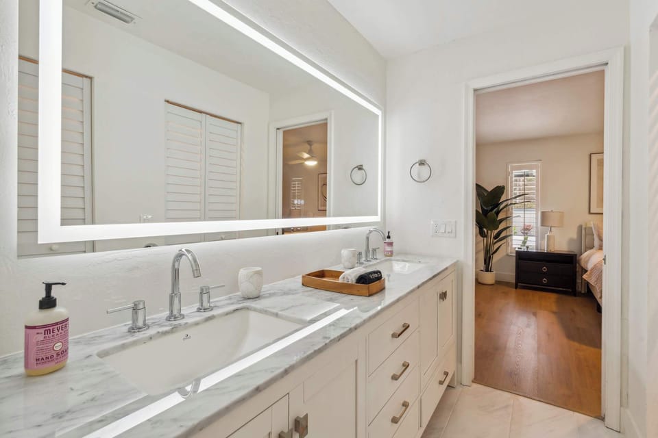 The en suite main bathroom has a large mirror with a light and 2 sinks in a large vanity 