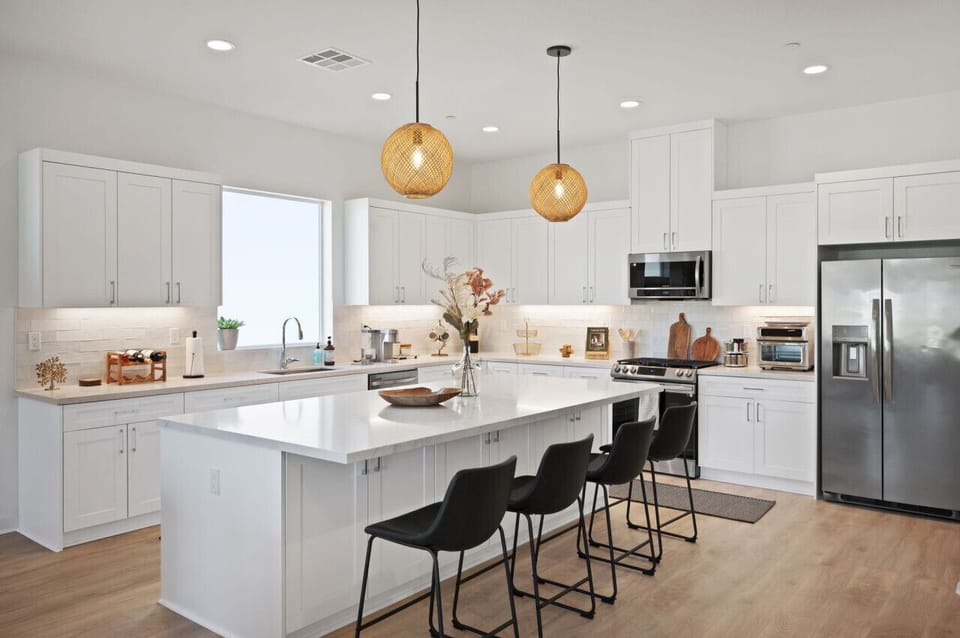Sleek white kitchen w/ a spacious island, pendant lighting & bar seating for casual meals.