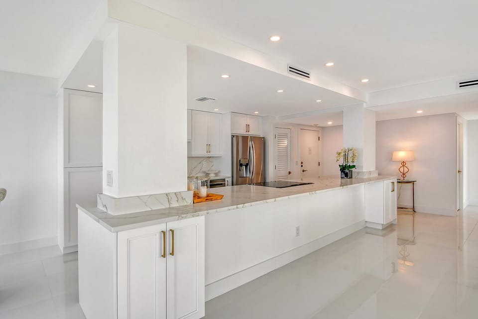 Open kitchen with marble countertops, white cabinetry, stainless steel appliances, and recessed lighting.