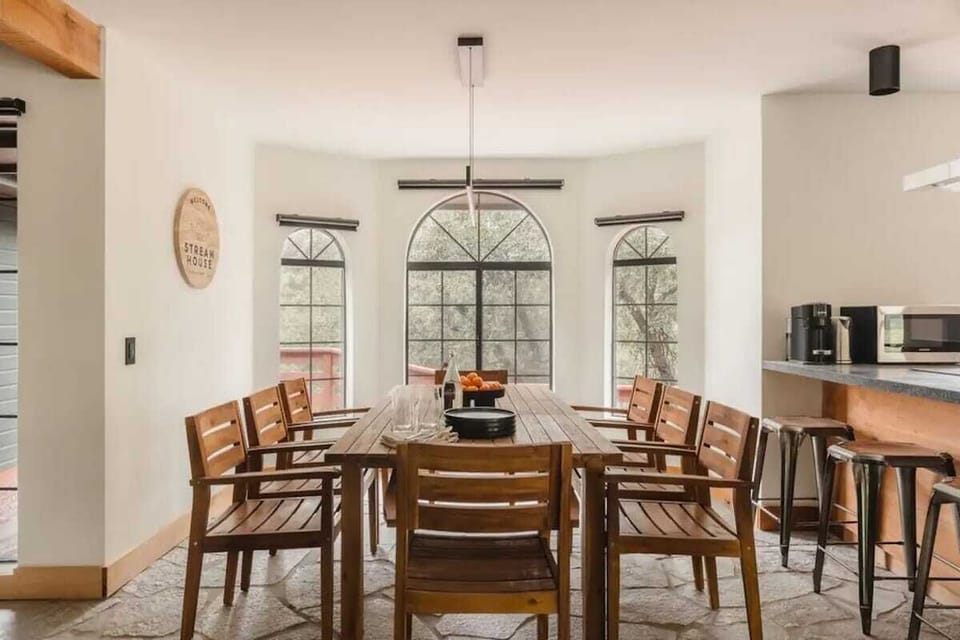A large dining area with eight seats, offers a serene and welcoming space for shared meals and gathering. The space is bathed in natural light thanks to the large, arched windows that provide beautiful views of the surrounding outdoor scenery.