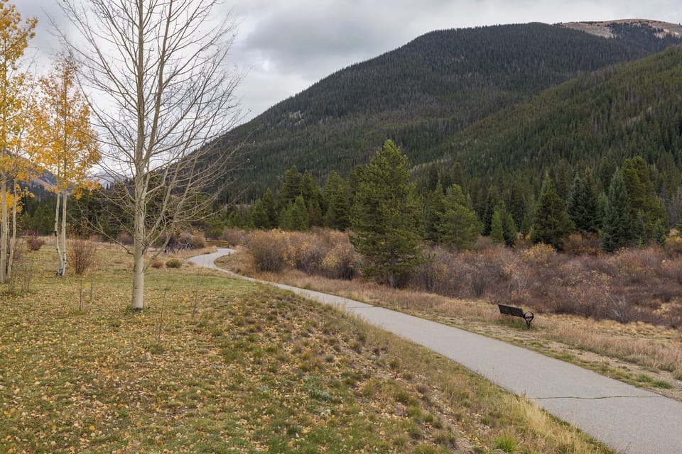 A scenic walking path winds through the autumn landscape toward forested mountains, perfect for peaceful morning strolls.
