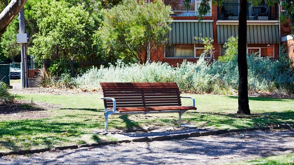 Take a book outside and enjoy the fresh air from a classic park bench tucked under a canopy of mature green trees.