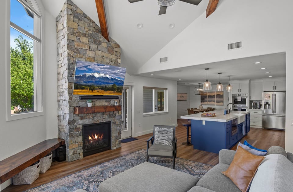 A stone gas fireplace anchors the room, surrounded by a plush L-shaped couch, a chaise lounge, and a wall-mounted TV.