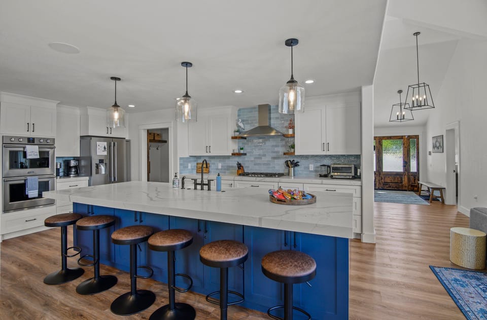 stunning white marbled quartz countertops and contrasting white and blue cabinetry hold a farmhouse sink, built-in microwave, dishwasher, double oven, gas stovetop, refrigerator, classic coffee machine, and Keurig
