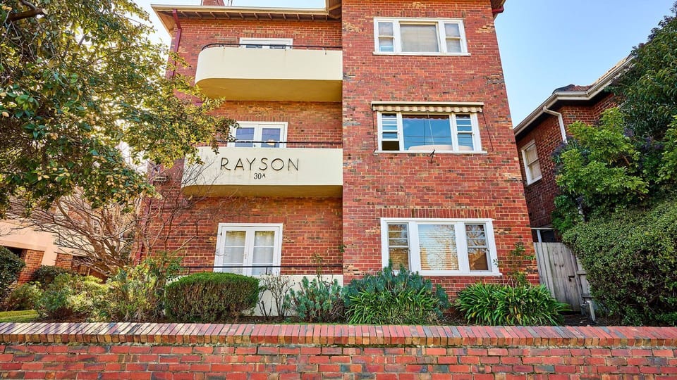 The striking facade of the "Rayson" building, showcasing timeless art deco style and manicured garden borders.