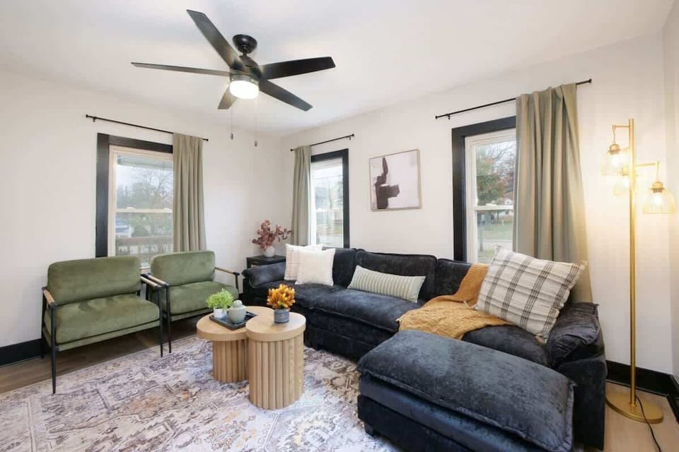 Sunlit living room w/ comfy seating, soft tones & large windows that brighten the space
