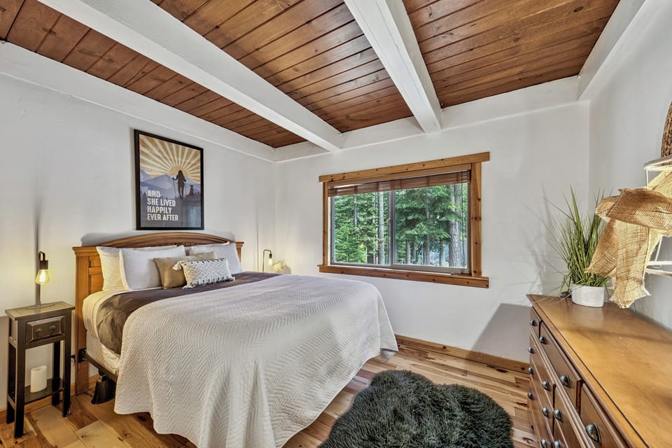 Relax under soaring wood-beamed ceilings in your cozy bedroom, where forest views and thoughtful decor create the perfect mountain retreat.