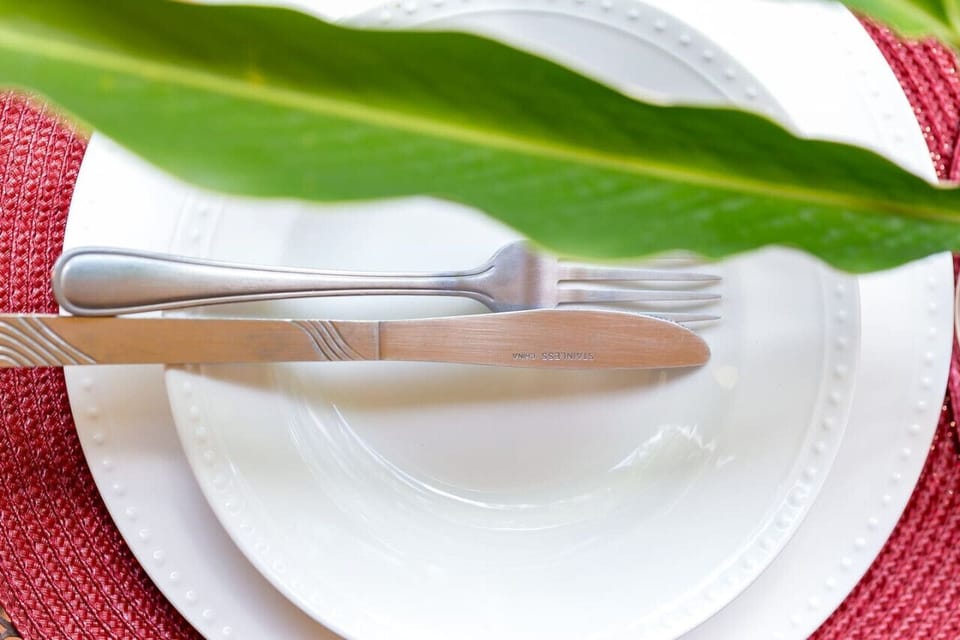 Simple table setting w/ plate, cutlery & tropical leaf accent for a welcoming touch.