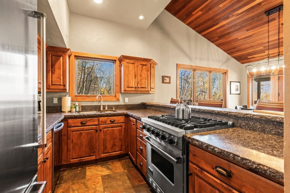 A fully-equipped kitchen, ideal for making meals or snacks. This kitchen has stainless steel appliances, wooden cabinets, and a small bar counter with seating. It’s perfect for groups who enjoy cooking