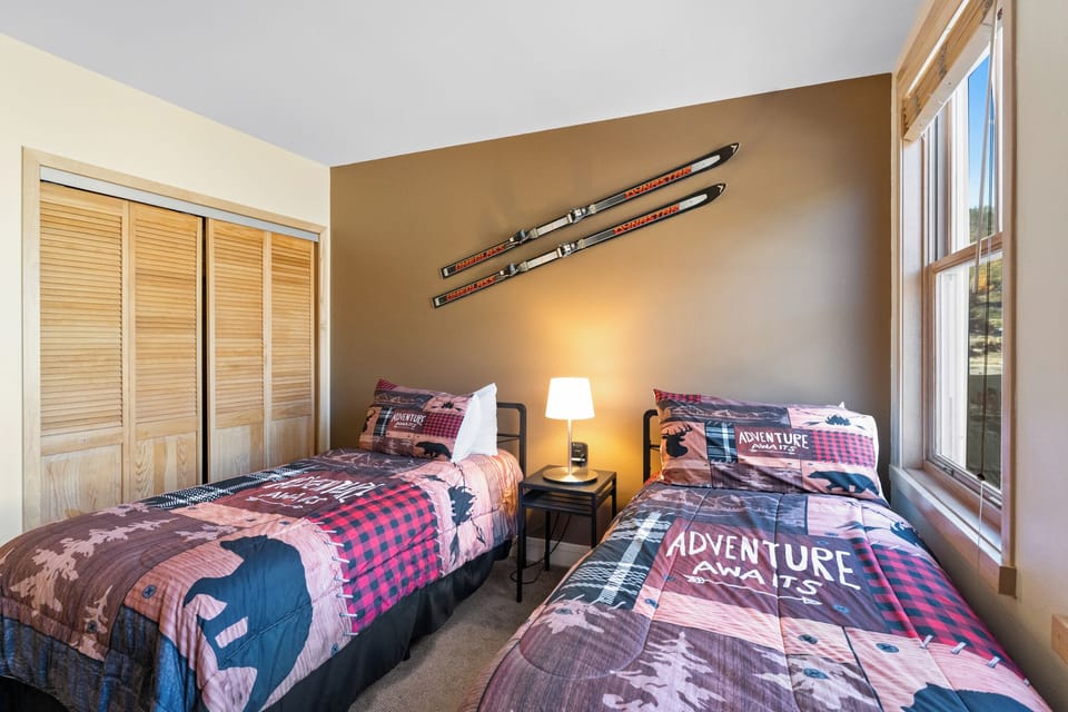 Cozy twin bedroom with adventure-themed bedding and vintage skis as decor. Your mountain getaway awaits with rustic charm and comfortable twin beds.
