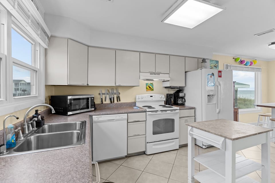 Oak Island, NC kitchen with white appliances, stove, sink, microwave, island cart, tile floors, beach décor, wood cabinet, and bright coastal style.