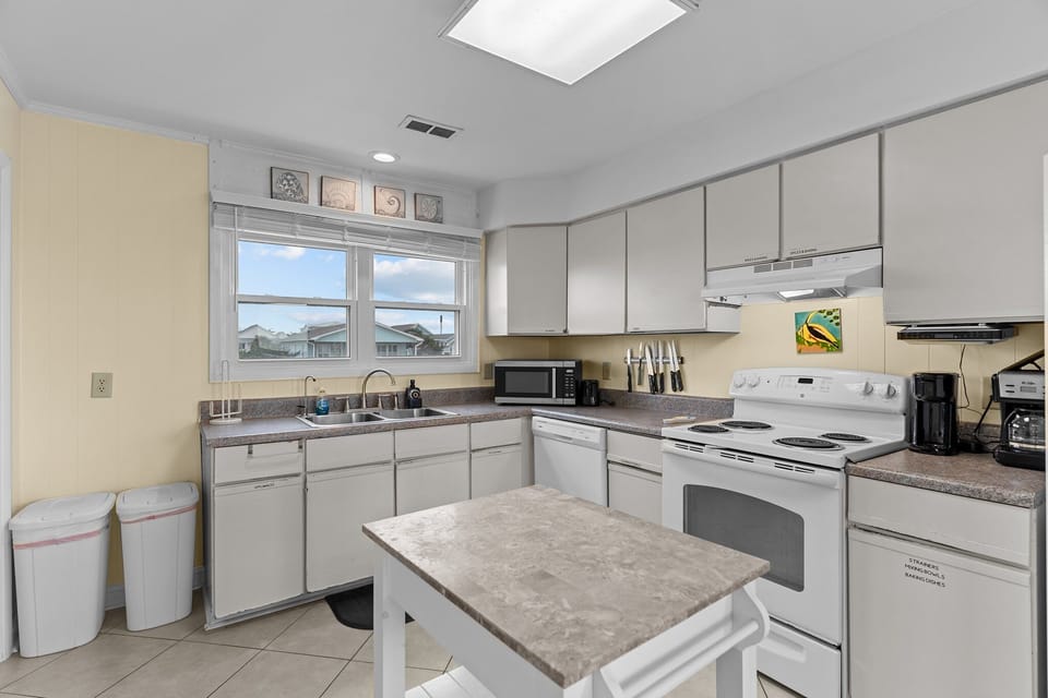 Oak Island, NC kitchen with white appliances, stove, sink, microwave, island cart, tile floors, beach décor, wood cabinet, and bright coastal style.