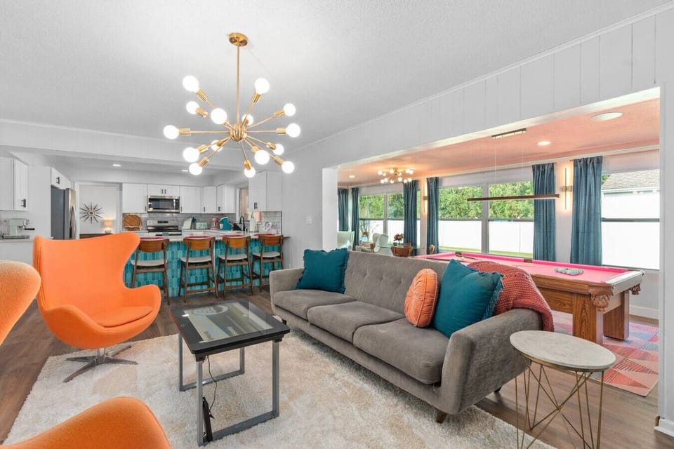Mid-century modern open living and dining with iconic orange egg chair, gold Sputnik chandelier, taupe sofa, teal accents and retro dining set, Vivid Vintage Orlando